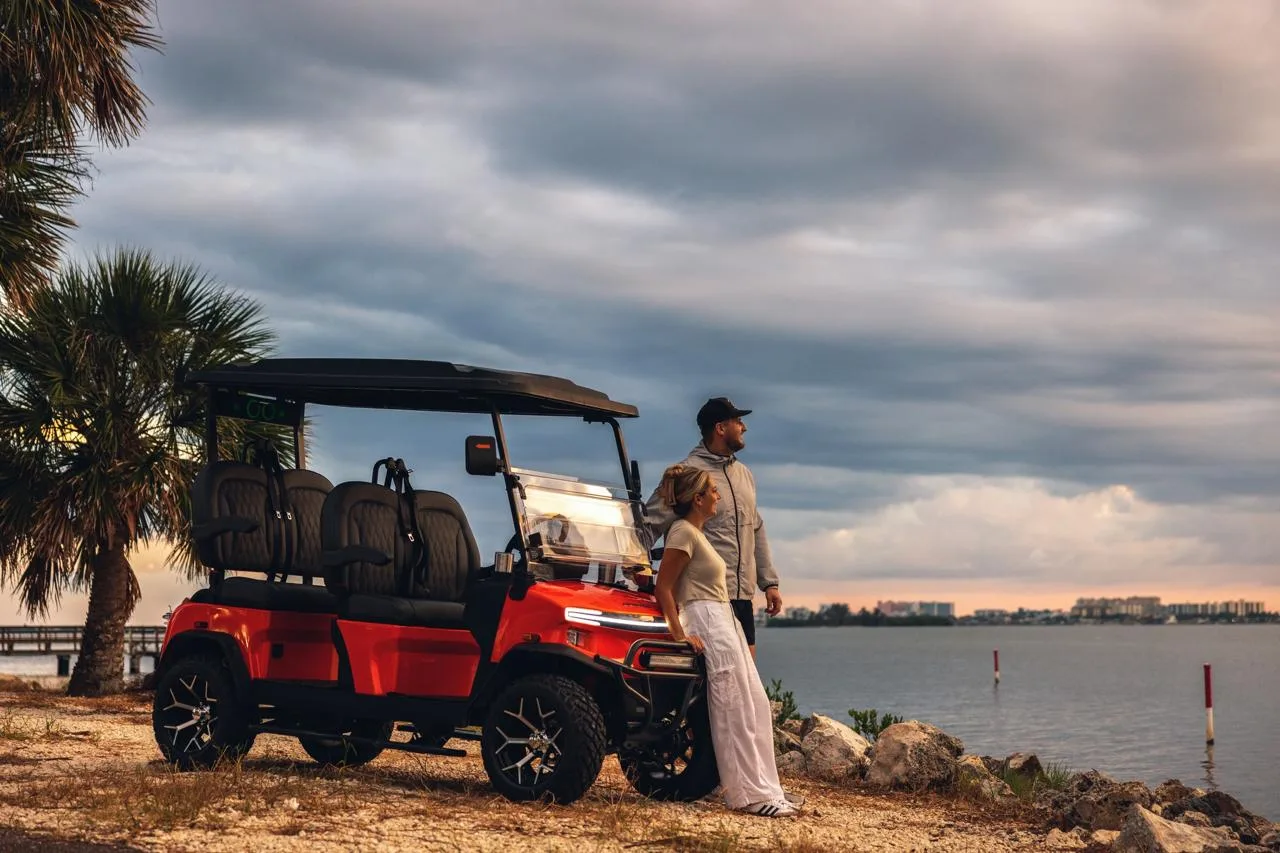 Carro de golf eléctrico Denago rojo con pareja en playa al atardecer